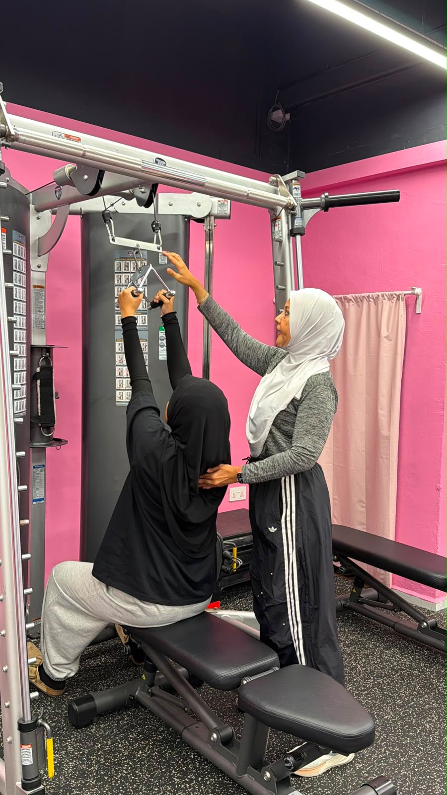 A FitFab.sg coach guiding a member through a cable machine exercise at the pink gym