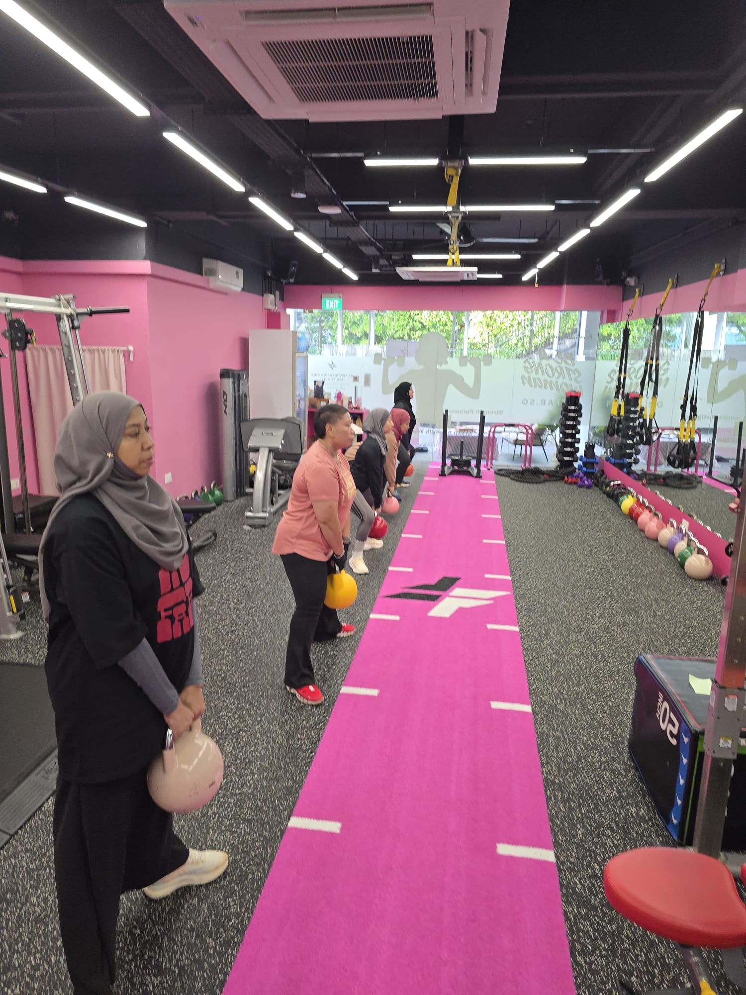 Women in a kettlebell group training session at the FitFab.sg pink gym