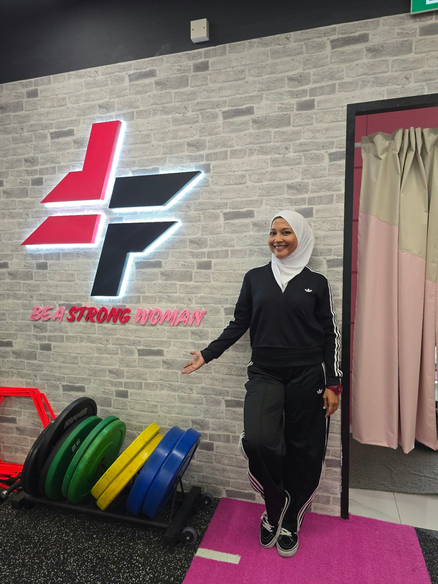 Haslinda Ali, founder of FitFab.sg, in front of the Be a Strong Woman logo wall at the pink gym